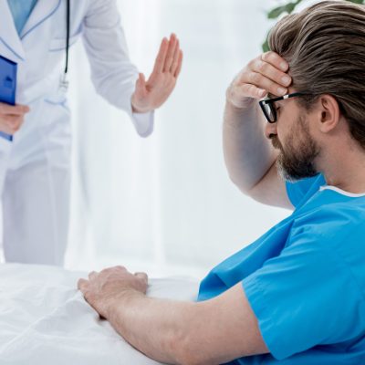 cropped view of doctor in white coat calming down sad patient in hospital