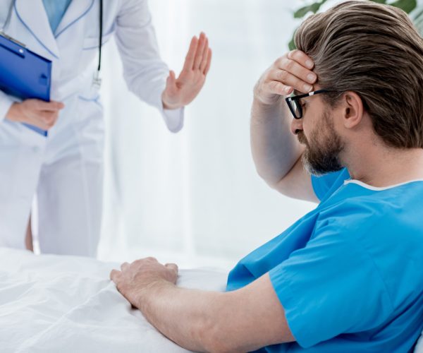 cropped view of doctor in white coat calming down sad patient in hospital